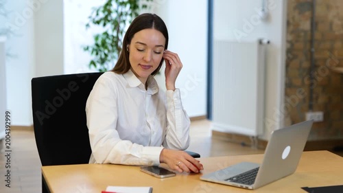 Relaxing work in a modern office. Realtime video. Caucasian beautiful female is sitting in front of her laptop and putting her earphones, and listening to music.