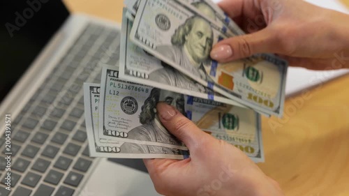 Real-time video.Female Caucasian hands with good nude manicures are counting cash money in front of the computer on the wooden contemporary office desktop.