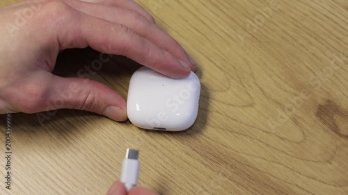 Man charging white wireless earbuds in a charging case.