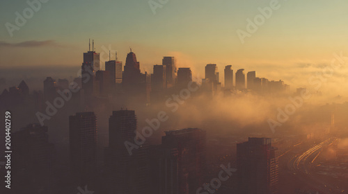 Dense fog covers urban cityscape at golden hour sunrise, with skyscrapers emerging through the mist and warm light.