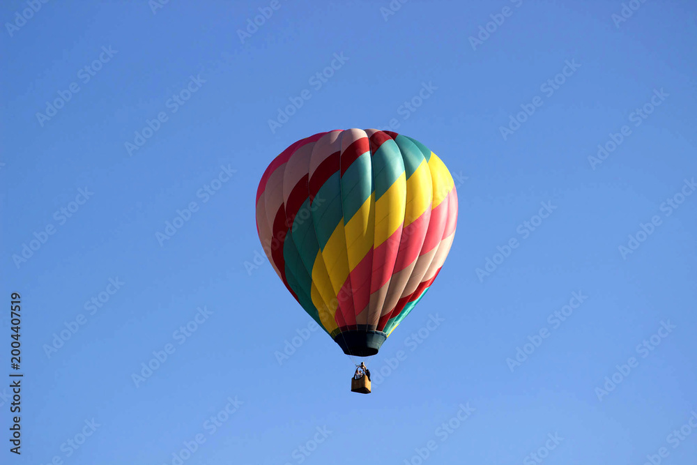 Naklejka premium Diagonal rainbow striped hot air balloon floating in clear blue sky