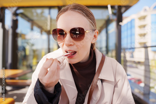 Woman eating dessert with spoon at outdoor cafe in sunlight