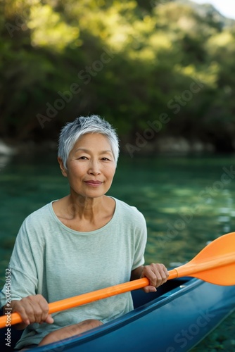 Older woman holding paddle while seated in kayak on lake near forest shore