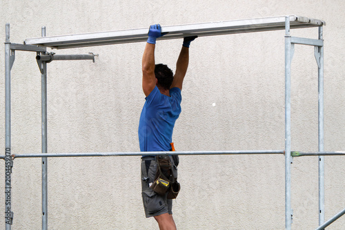 Fotografie Craftsman dismantling scaffolding professionally in front of building wall