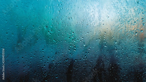 Fotografie Blue rain drops on window glass with abstract ocean water texture and nature lig