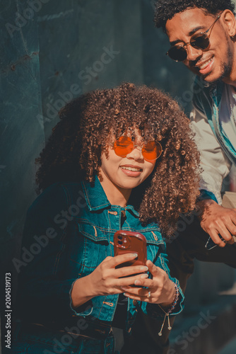 Obraz na płótnie Young stylish couple sharing a fun moment looking at a smartphone outdoors, smil