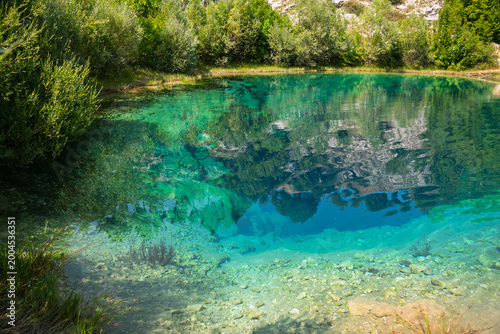 Deep turquoise karst spring with crystal clear water reflecting green vegetation and rocky cliffs