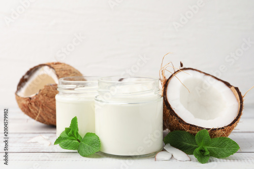 Tableau sur toile Delicious coconut yogurt in glass jars, mint leaves and fruits on white wooden t