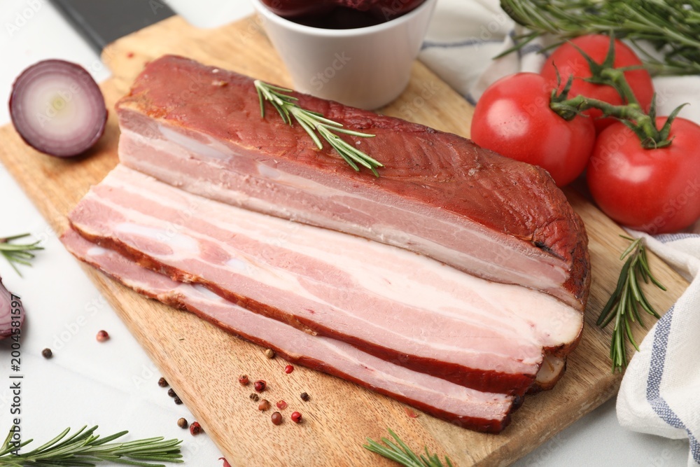 Fototapeta premium Pieces of smoked bacon with peppercorns, rosemary, onion and tomatoes on white table, closeup