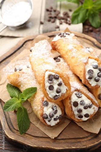 Foto Delicious cannoli with cheese, chocolate chips, powdered sugar and mint on woode