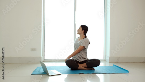 Fotografia Woman practicing seated spinal twist yoga pose at home with laptop for online fi