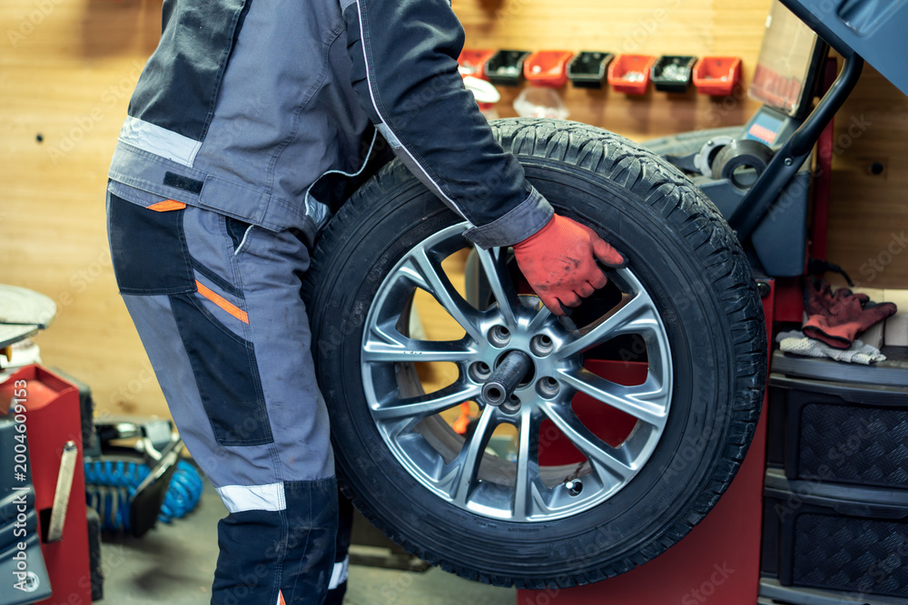 Obraz premium Worker changes a tire at a garage during the day in an auto repair shop in the city