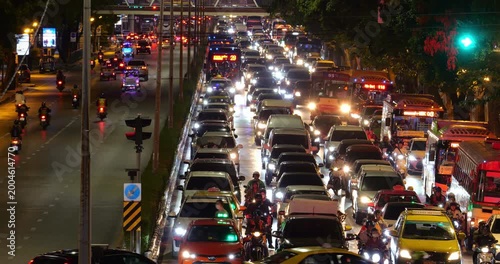 Nighttime view of congested arterial road in Bangkok, with countless cars, motorcycles, and buses in congestion at ongoing lanes, outgoing lanes are empty