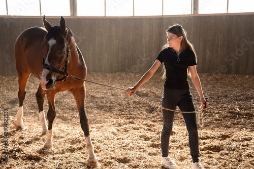 Fényképezés Teenage girl leading her horse horse bridle in indoor arena during training