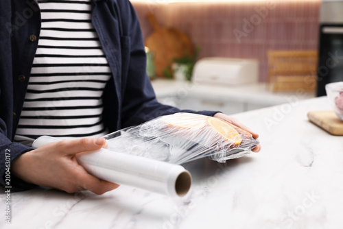 Foto Woman wrapping container with fresh orange slices in cling film at light marble