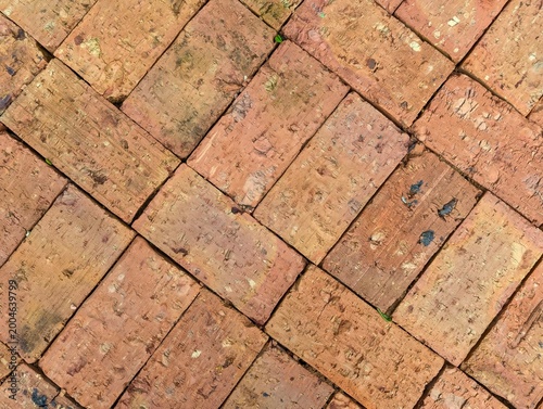 Top view of rustic red brick pavement in a herringbone pattern, weathered clay brick texture for architectural background and outdoor flooring design.