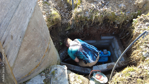 Person works on a water pump in a deep well during a sunny afternoon in a rural area