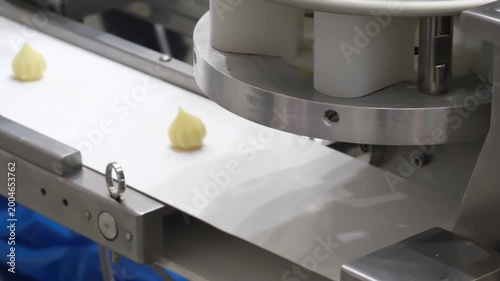 Freshly formed pastry shapes move along a conveyor belt in a modern bakery. The golden-brown dough pieces sit neatly aligned, ready for baking