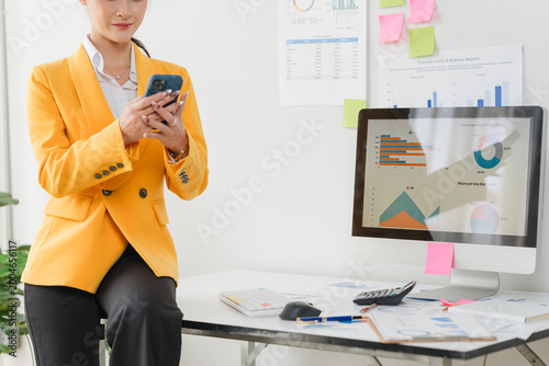 Using mobile, cheerful young asian business woman working at working place.