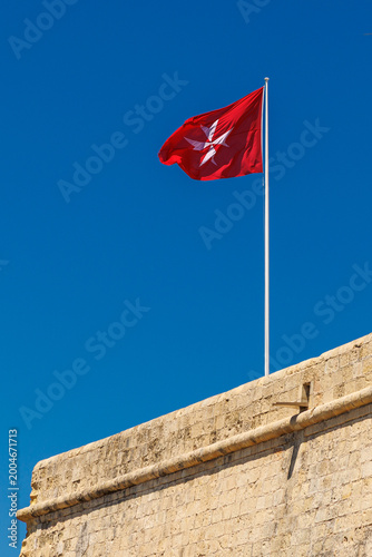 Canvastavla Maltese flag waving on a pole atop a stone fortification wall