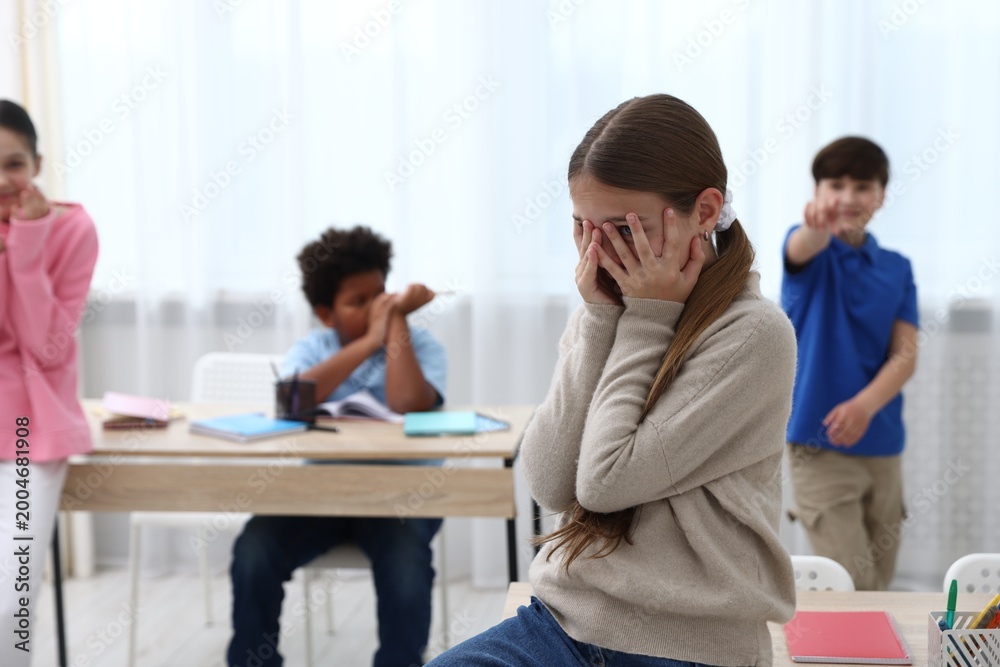 Fototapeta premium Girl getting bullied by her classmates in classroom, selective focus