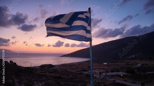 Beautiful view of a colourful sunrise at the Theodoti beach in Ios Greece, and the Greek flag waving in the air