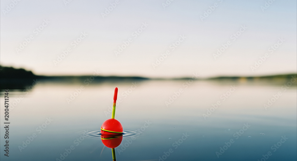 Fototapeta premium Fishing float bobbing on calm lake at golden hour with reflection, serene outdoor hobby concept