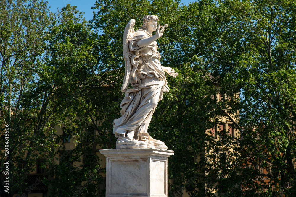 Fototapeta premium Marble angel statue on Ponte Sant Angelo bridge in Rome Italy isolated against green trees background with clear daylight