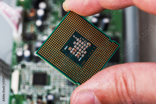 Macro close up of cpu processor chip with pins held by fingers over motherboard