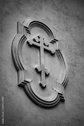 Religious cross symbol relief carving on textured stone wall