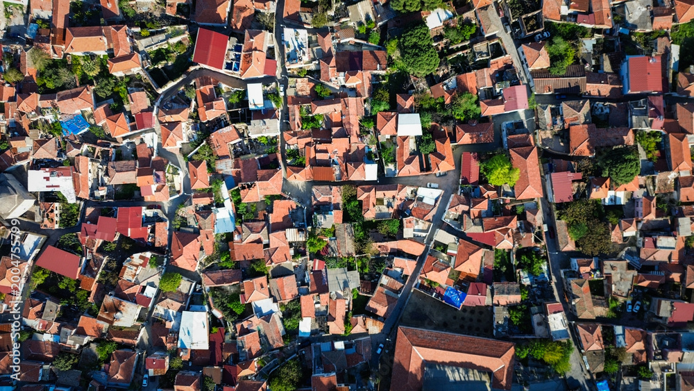 Fototapeta premium Aerial drone view of Bergama, Izmir, Turkey, showing dense urban neighborhoods, red-roofed houses, surrounding farmland, hills, and a wide Aegean landscape.