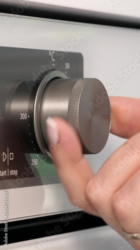 Woman adjusting modern oven in kitchen. Female hand pushing and turning knobs on oven control panel. Closeup. Vertical footage
