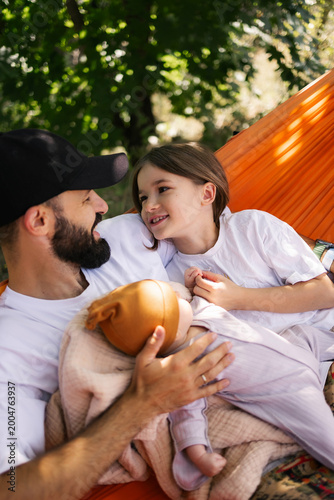 Father and daughter share warm moment together while holding baby in outdoor tent surrounded by trees