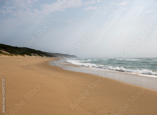 Wide sandy beach with ocean waves under cloudy sky in peaceful coastal landscape and natural seaside scenery