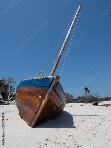 Weathered Wooden Sailboat Resting on a Tropical Sandy Beach
