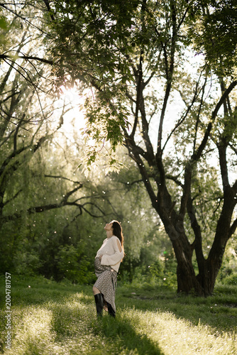 Woman stands in sunlit forest breathing fresh air feeling calm and peaceful among tall trees and green grass