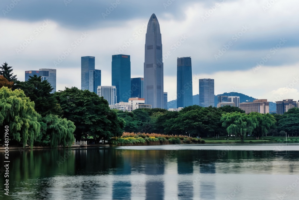 Fototapeta premium Tall modern skyscrapers rise above green parkland and calm lake. Cityscape with trees and water reflection shows urban development. Nature meets city buildings in harmonious skyline.