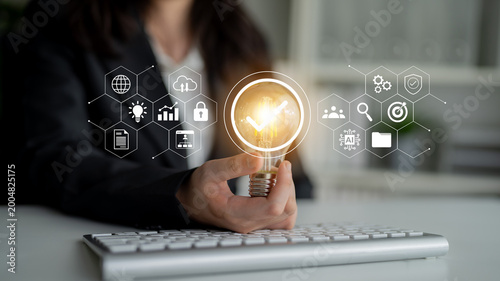 Fotografie A business professional holds a light bulb symbolizing innovative ideas amidst digital graphics representing technology and growth strategies in a modern office environment