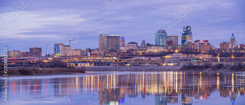 The Kansas City skyline glows at dusk beside the river.