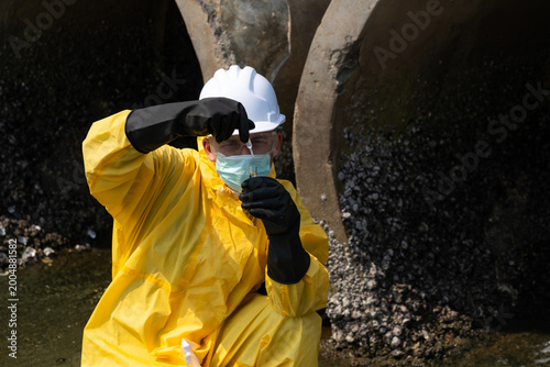 Schilderij op canvas Environmental engineers, wearing yellow chemical protective suits and helmets, are collecting water samples from sewers to check for pollution and environmental quality