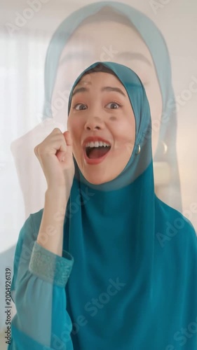 Joyful young woman wearing teal hijab and dress, smiling brightly in a well-lit indoor setting with soft natural light