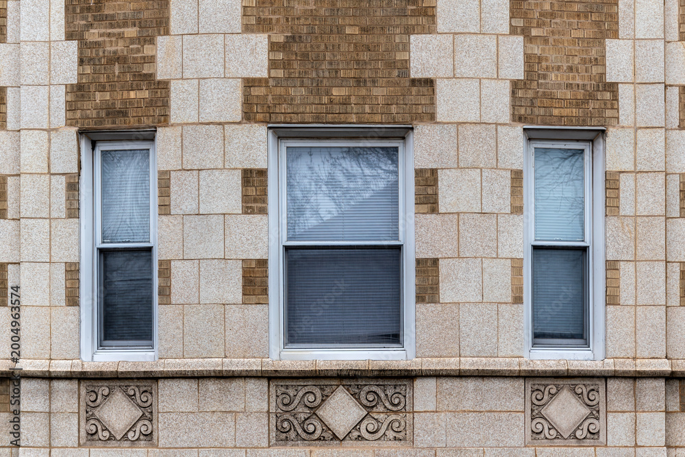 Fototapeta premium Three rectangular windows on a brick wall clad in beige tiles, with bas-reliefs beneath the windows. From the Windows of the world series.