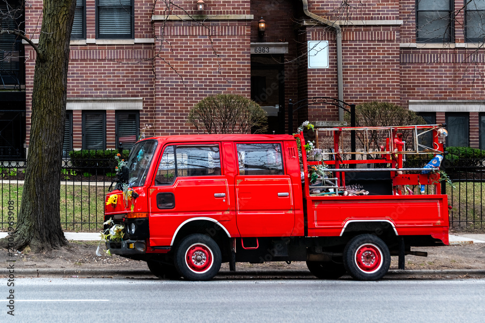Fototapeta premium Small red truck was parked on one of the streets in Chicago, across from a red-brick house.