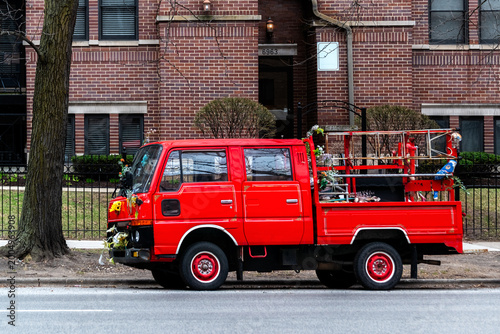 Small red truck was parked on one of the streets in Chicago, across from a red-brick house.
