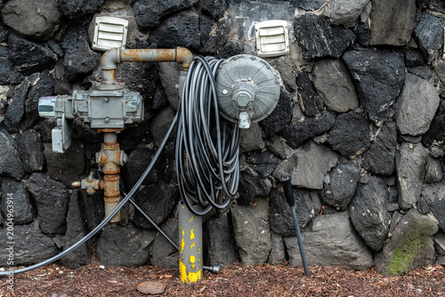 Gas supply system for a residential building, set against a cobblestone wall, with a flexible gray water supply hose.
