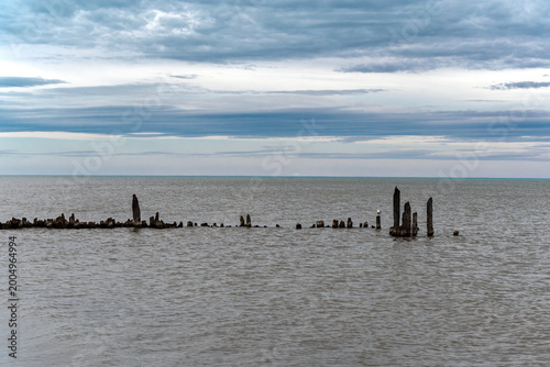Old wooden beams protrude from the water at the site of an old pier on Lake Michigan, against a backdrop of gray skies.