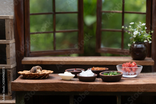 Cooking ingredients and seasonings placed on a wooden counter in front of a rustic window with a garden view.