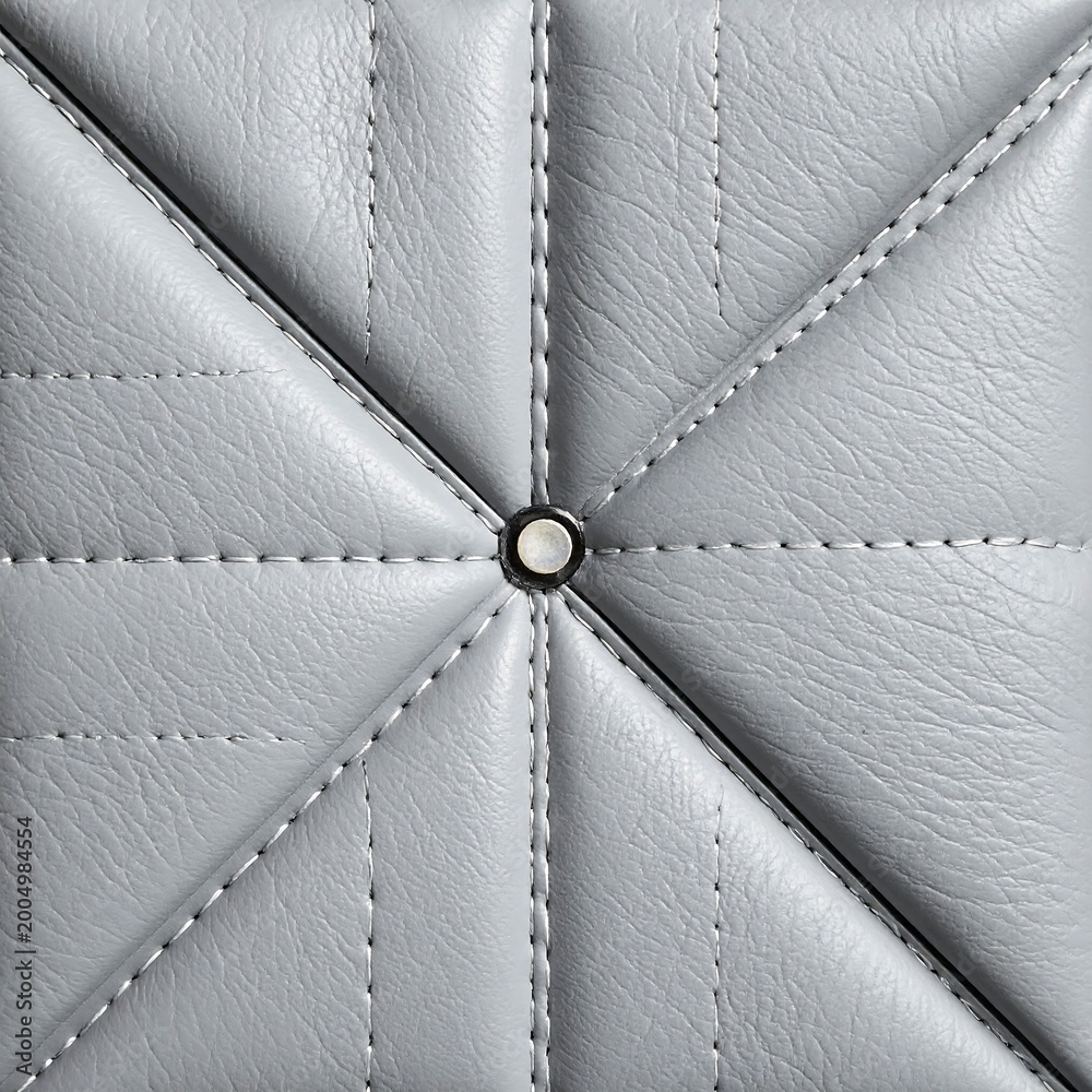 Fototapeta premium Close-up of a square quilted surface in a pale gray tone, featuring diamond-shaped patterns with centered metallic detail