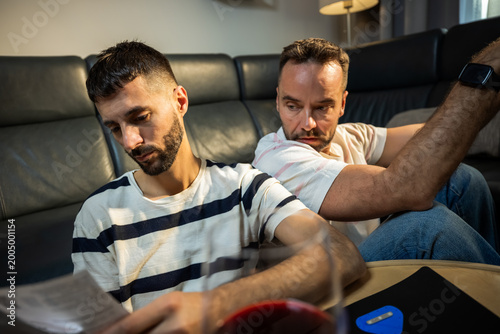 Fotografía Exhausted gay couple feeling overwhelmed by debt and pile of bills