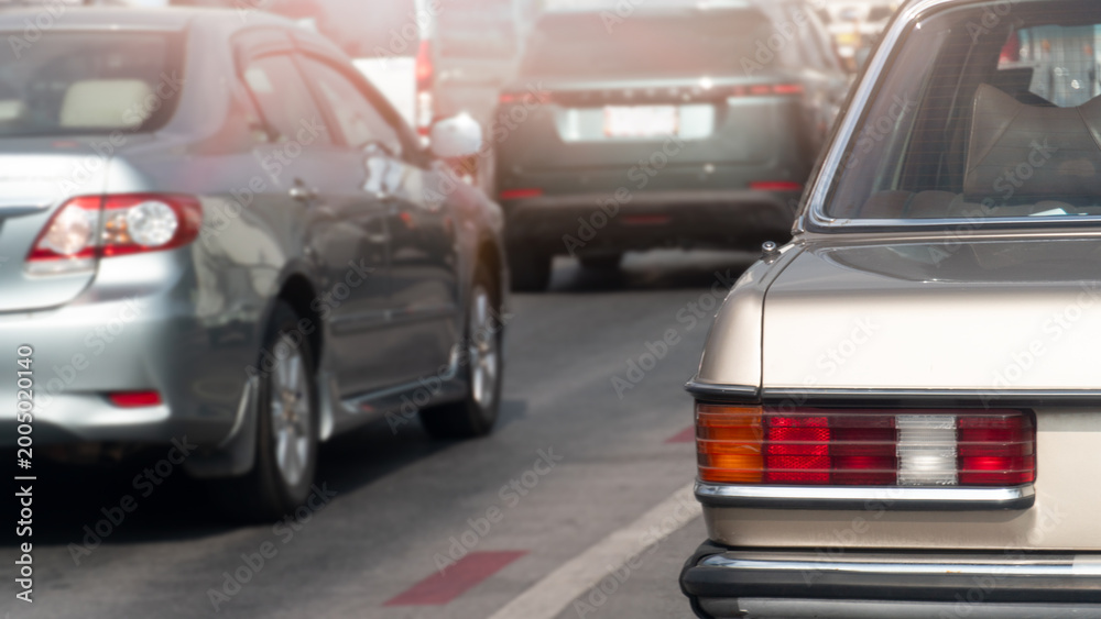 Fototapeta premium Rear side of classic car soft gold color driving on asphalt road. Side of car with other cars driving flanking at day time.